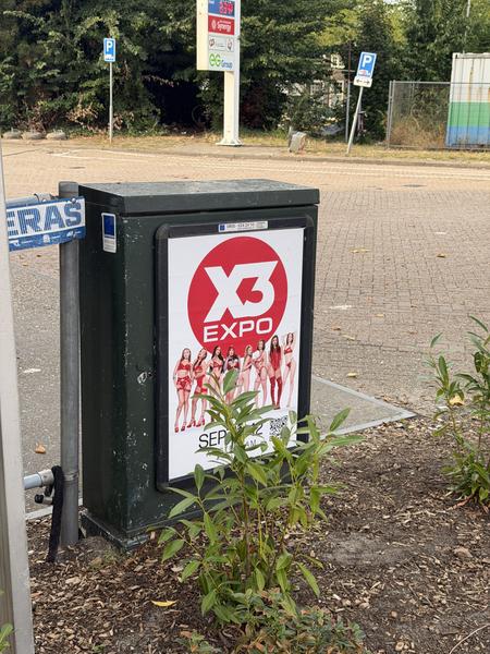 This photo captures a street scene at Sarphatistraat, Kadijken, Amsterdam, featuring an electrical box with a prominent 'X3 EXPO' advertisement